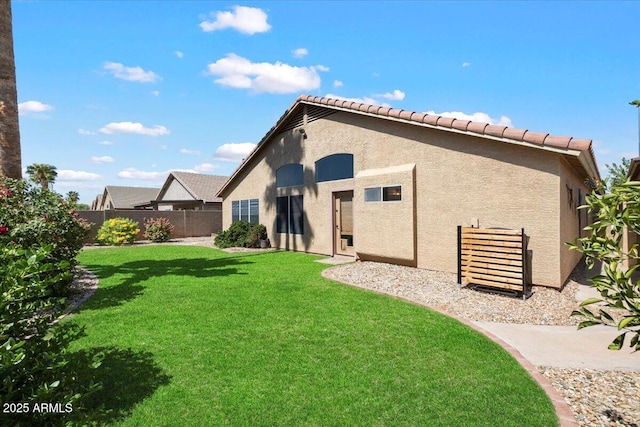 rear view of property with fence, stucco siding, a yard, and a tile roof