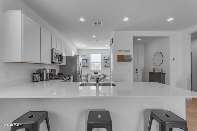 kitchen with sink, stainless steel appliances, kitchen peninsula, a breakfast bar area, and white cabinets