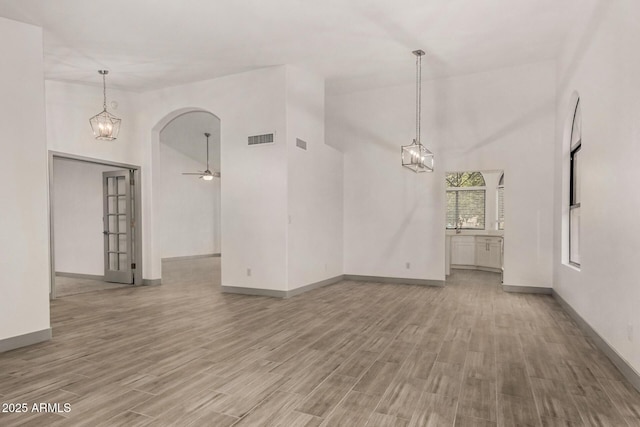 empty room featuring visible vents, ceiling fan with notable chandelier, light wood-style floors, arched walkways, and high vaulted ceiling