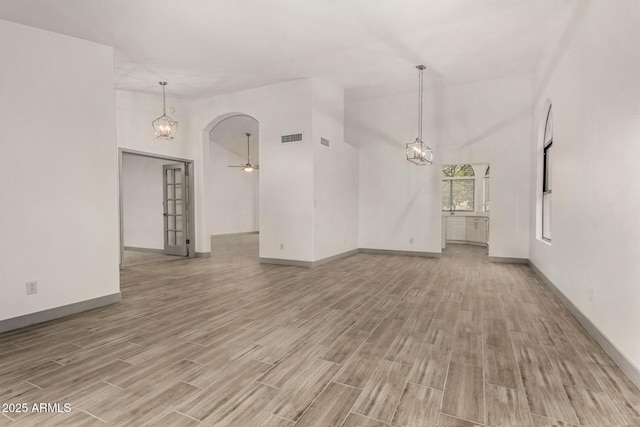 empty room with baseboards, visible vents, high vaulted ceiling, ceiling fan, and light wood-type flooring