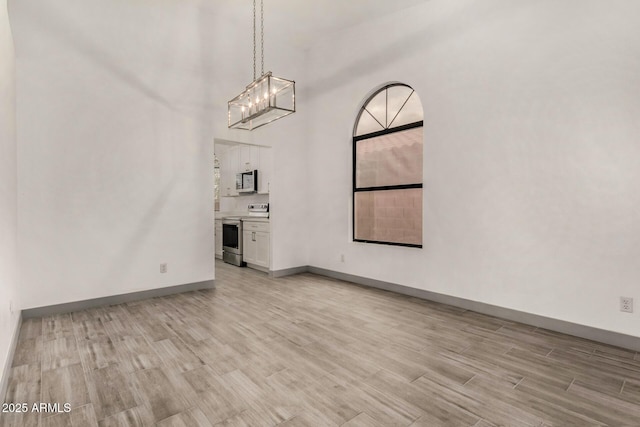 interior space with baseboards, a high ceiling, an inviting chandelier, and light wood-style flooring