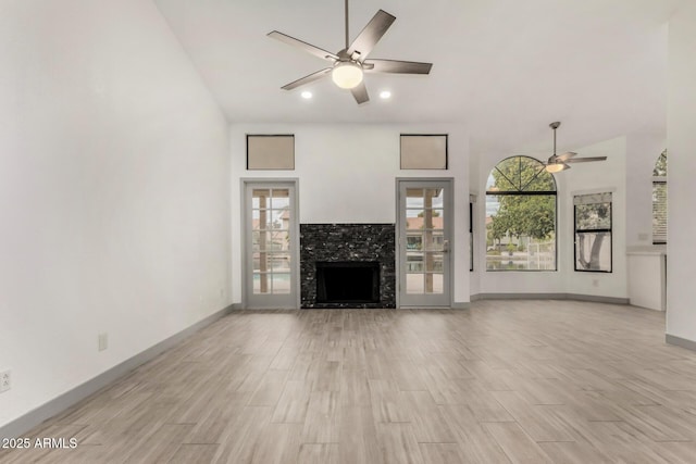 unfurnished living room with baseboards, ceiling fan, a fireplace, and light wood finished floors