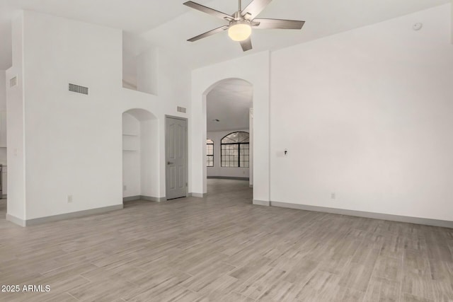 unfurnished room featuring light wood finished floors, visible vents, baseboards, arched walkways, and a ceiling fan