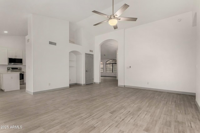 unfurnished living room with high vaulted ceiling, a ceiling fan, arched walkways, and light wood-type flooring