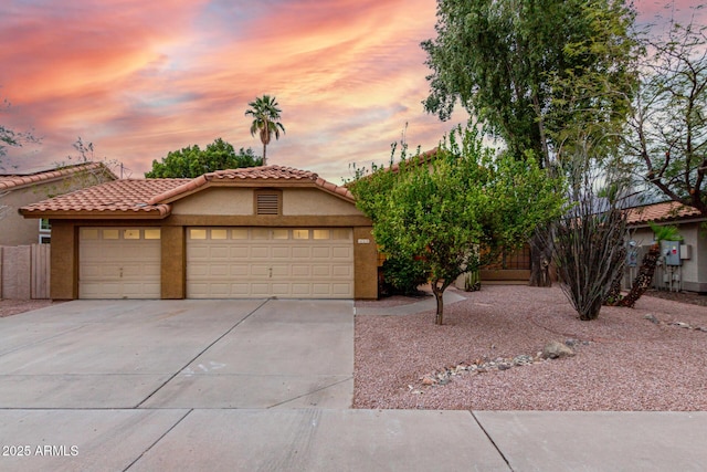 view of front facade with fence, a tile roof, stucco siding, a garage, and driveway