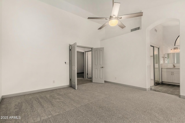 unfurnished bedroom featuring arched walkways, carpet flooring, a high ceiling, and a sink