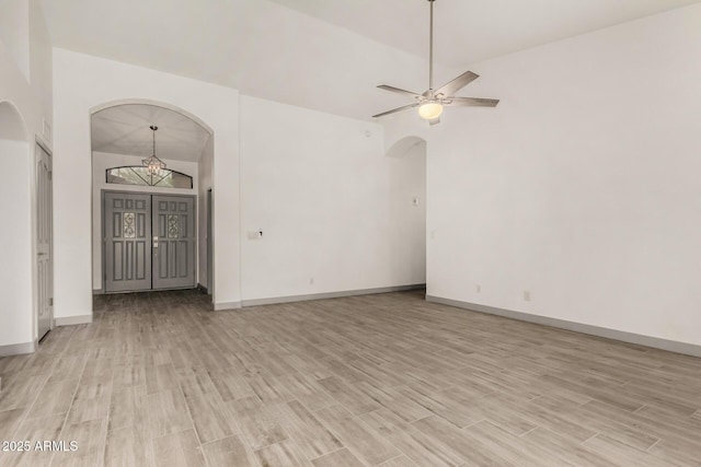 unfurnished room featuring baseboards, arched walkways, and light wood-type flooring