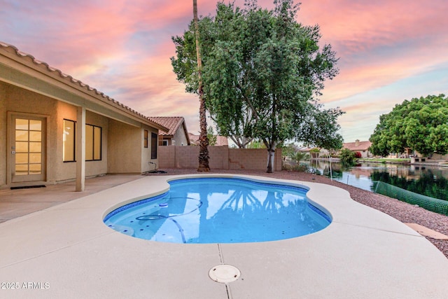 pool at dusk with a patio area, a fenced backyard, a fenced in pool, and a water view