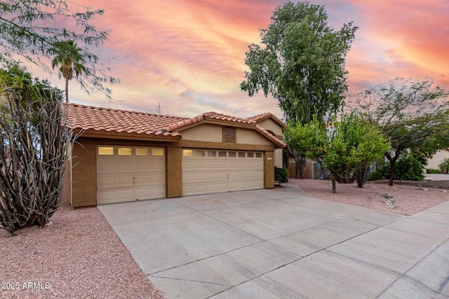 mediterranean / spanish-style house with a tiled roof, an attached garage, driveway, and stucco siding