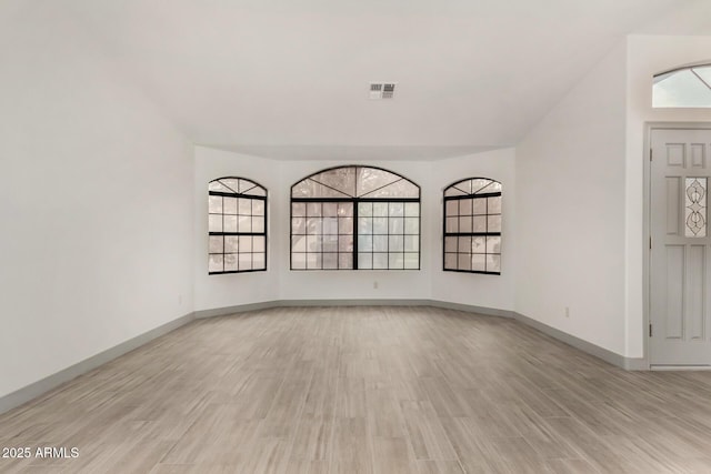 spare room with light wood-type flooring, visible vents, and baseboards