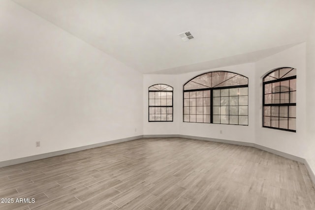 unfurnished room with visible vents, baseboards, light wood-style floors, and vaulted ceiling