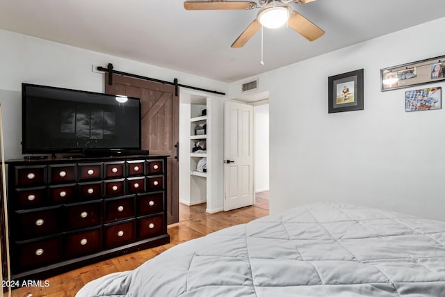 bedroom featuring ceiling fan, a barn door, and light wood-type flooring