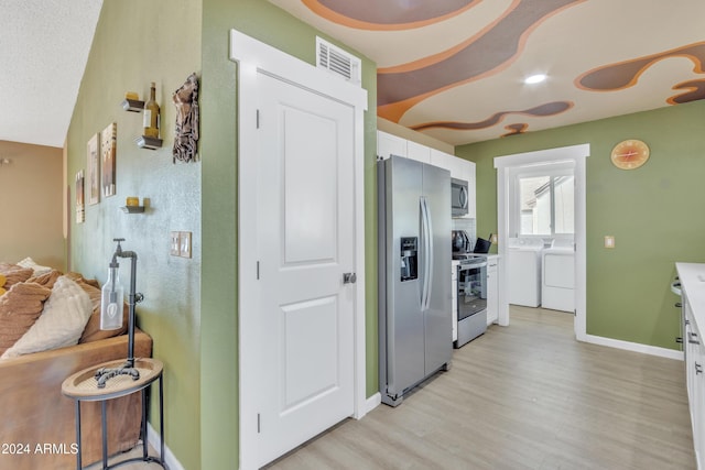 kitchen featuring white cabinetry, stainless steel appliances, washing machine and dryer, light hardwood / wood-style flooring, and vaulted ceiling