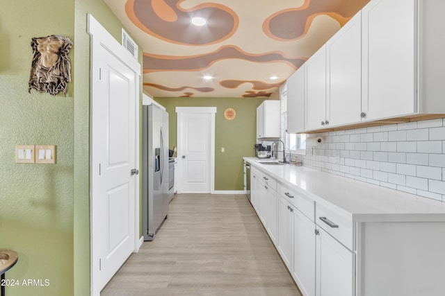 kitchen featuring sink, light hardwood / wood-style flooring, decorative backsplash, white cabinetry, and stainless steel appliances