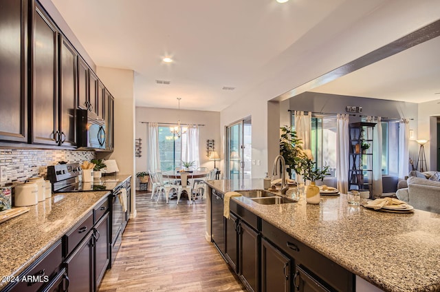 kitchen featuring electric range, sink, hanging light fixtures, an inviting chandelier, and light stone counters