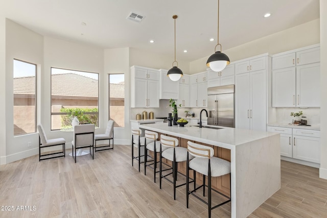 kitchen with light countertops, decorative backsplash, white cabinetry, a sink, and built in refrigerator