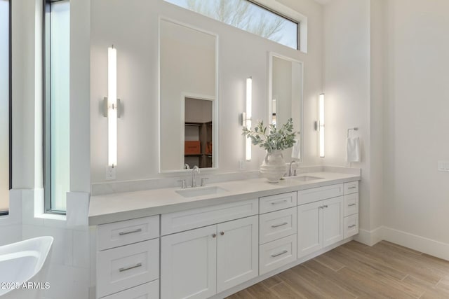 full bathroom with a soaking tub, double vanity, a sink, and wood finished floors