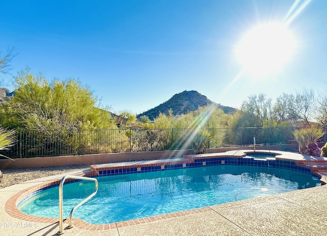 view of swimming pool featuring a pool with connected hot tub, fence, and a mountain view