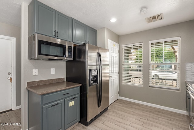 kitchen featuring gray cabinetry, light wood-type flooring, a textured ceiling, and appliances with stainless steel finishes