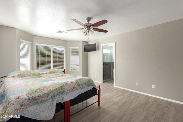 bedroom featuring ceiling fan, a textured ceiling, light wood-type flooring, and ensuite bath