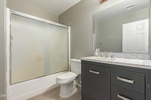 full bathroom featuring wood-type flooring, tasteful backsplash, combined bath / shower with glass door, vanity, and toilet