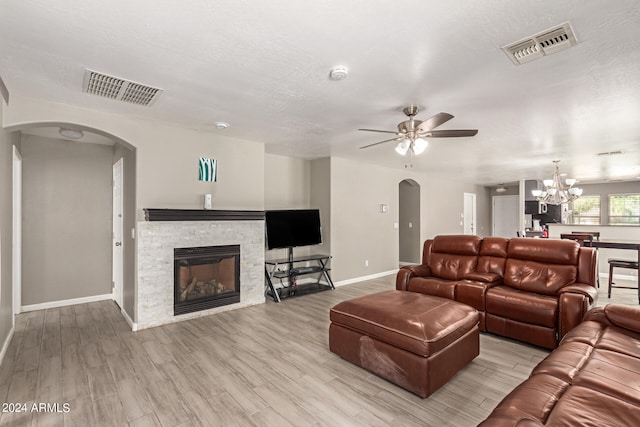 living room with a stone fireplace, a textured ceiling, ceiling fan with notable chandelier, and light wood-type flooring