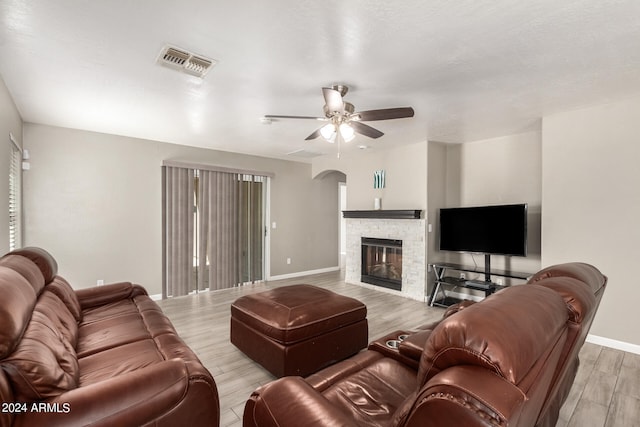 living room with light hardwood / wood-style flooring, ceiling fan, and a stone fireplace