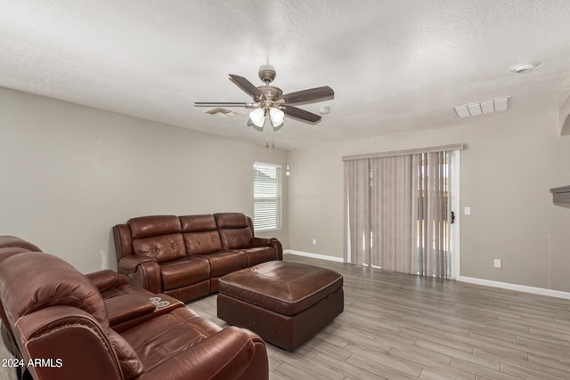 living room with a textured ceiling, ceiling fan, and light hardwood / wood-style flooring