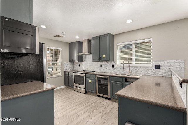 kitchen with sink, beverage cooler, wall chimney range hood, gray cabinets, and stainless steel range