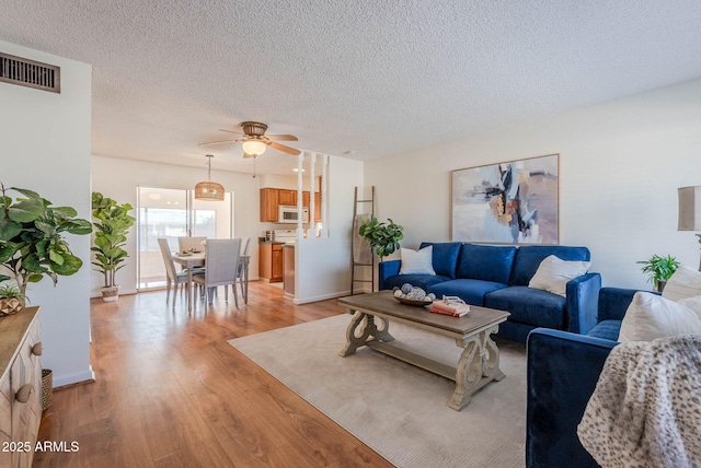 living room with light wood-type flooring, ceiling fan, and a textured ceiling