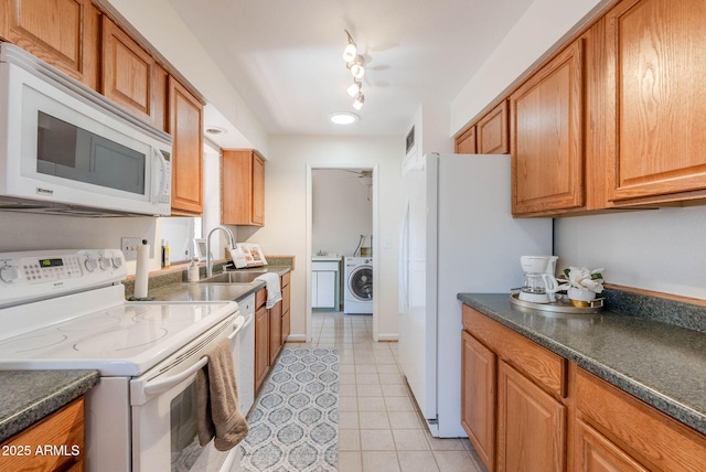 kitchen with dark stone countertops, washer / dryer, light tile patterned flooring, sink, and white appliances