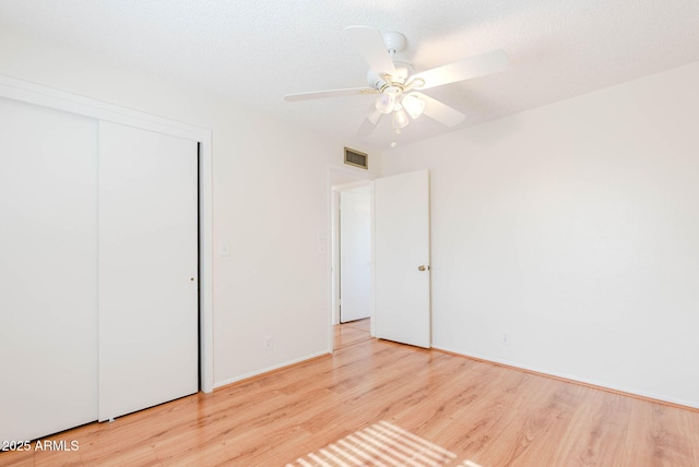 unfurnished bedroom with ceiling fan, a textured ceiling, a closet, and light wood-type flooring