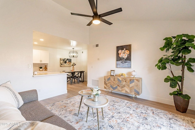 living room featuring light hardwood / wood-style floors, ceiling fan with notable chandelier, and high vaulted ceiling