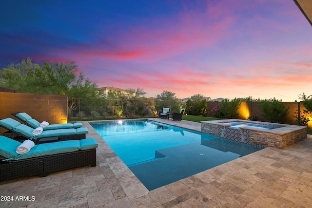 pool at dusk featuring a patio area and an in ground hot tub