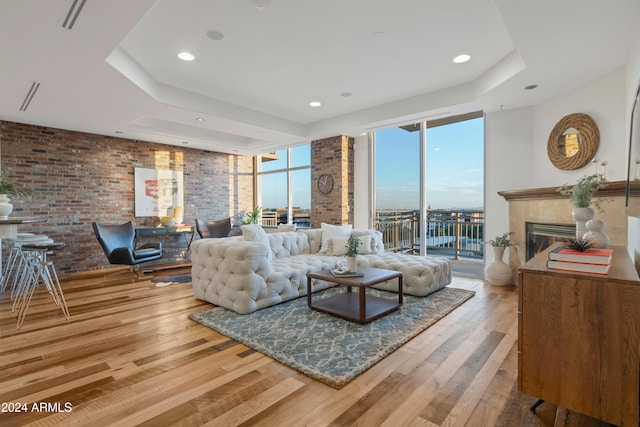 living room featuring brick wall, a raised ceiling, hardwood / wood-style flooring, a wall of windows, and a fireplace