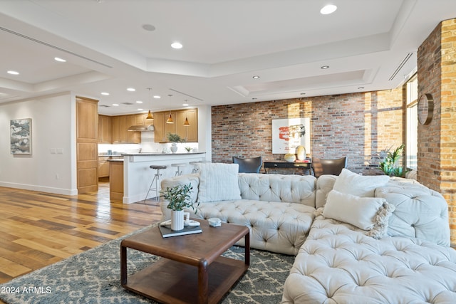 living room featuring a raised ceiling, light hardwood / wood-style floors, and brick wall