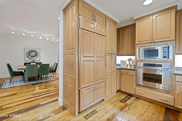 kitchen featuring built in appliances, light brown cabinetry, dark stone counters, and light wood-type flooring