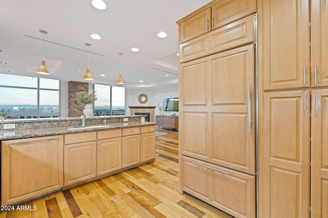 kitchen with dark stone countertops, hanging light fixtures, light hardwood / wood-style floors, and light brown cabinets