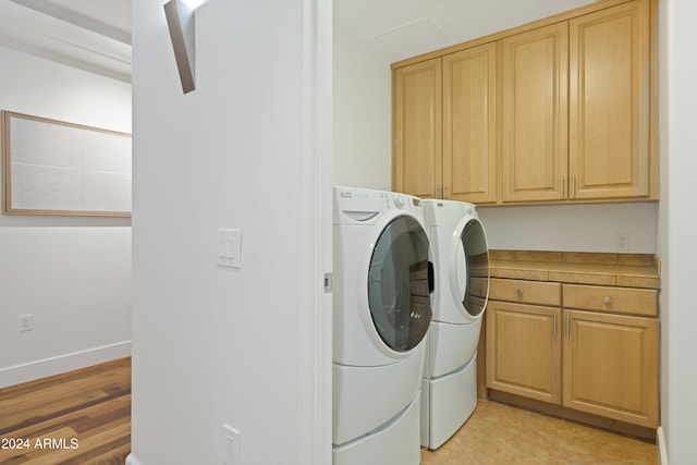 clothes washing area with cabinets, washing machine and dryer, and light hardwood / wood-style floors