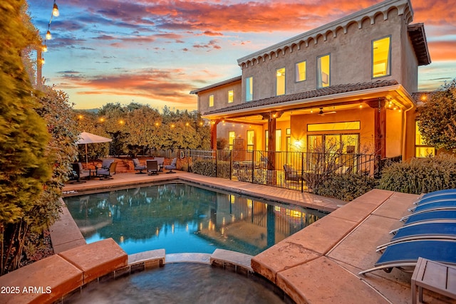 pool at dusk featuring an in ground hot tub, ceiling fan, and a patio area