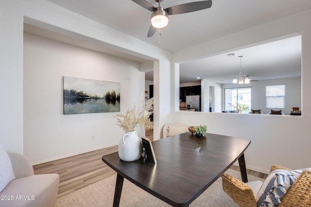 dining space featuring ceiling fan with notable chandelier, light wood finished floors, and baseboards