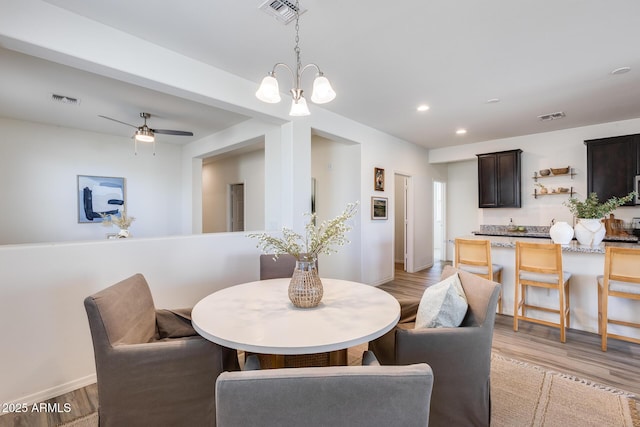 dining space with ceiling fan with notable chandelier and light wood-type flooring