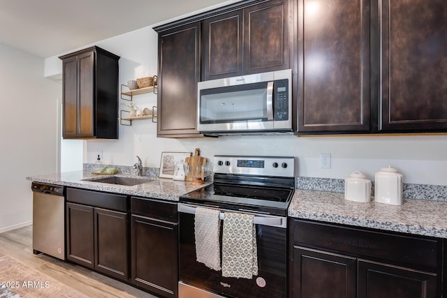 kitchen featuring light wood finished floors, light stone counters, appliances with stainless steel finishes, open shelves, and a sink