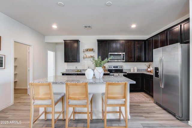 kitchen with light stone countertops, dark brown cabinets, stainless steel appliances, and a kitchen island