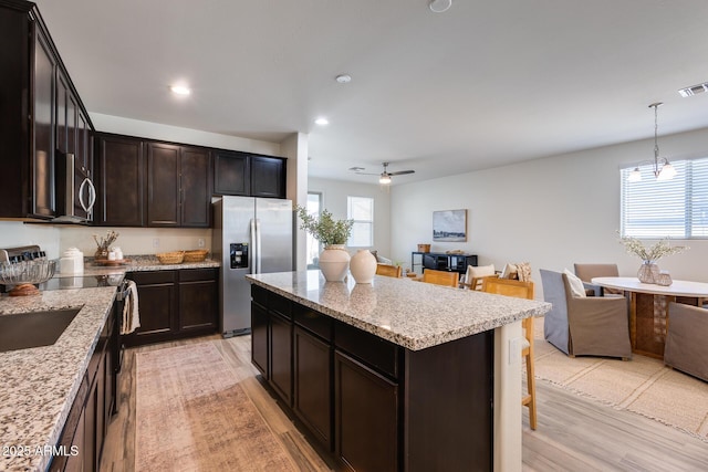 kitchen with a center island, stainless steel appliances, light wood-style flooring, open floor plan, and light stone countertops