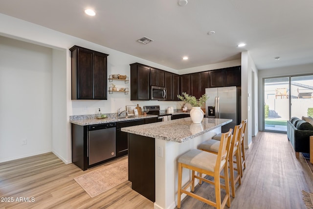 kitchen featuring light stone counters, stainless steel appliances, visible vents, dark brown cabinets, and light wood finished floors