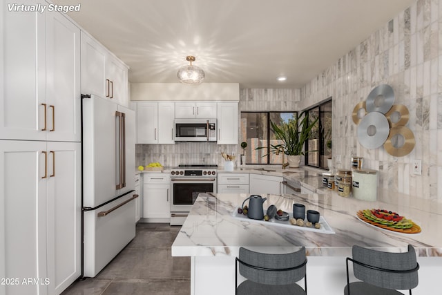 kitchen featuring light stone countertops, white appliances, white cabinets, a kitchen bar, and pendant lighting