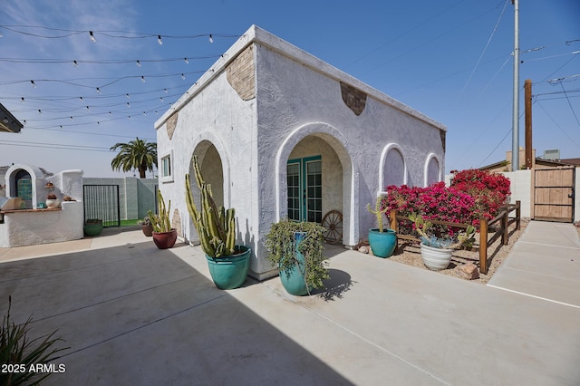 view of side of property with a patio area, a gate, fence, and stucco siding