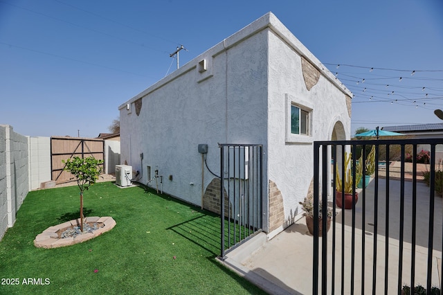 view of side of home with a lawn, a fenced backyard, a gate, central AC, and stucco siding