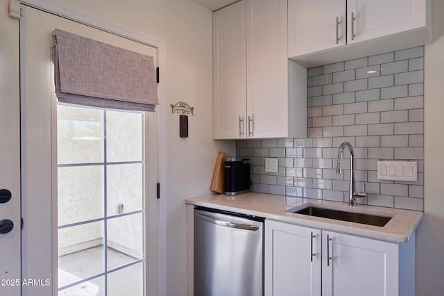 kitchen featuring decorative backsplash, stainless steel dishwasher, white cabinetry, a sink, and light stone countertops